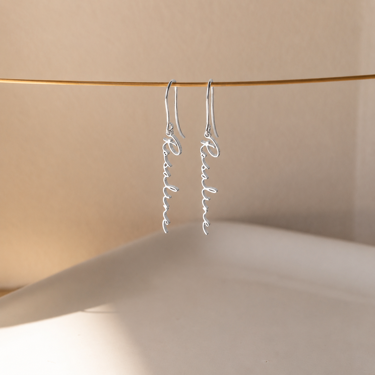 Silver earrings with 'Pauline' inscription on a beige background